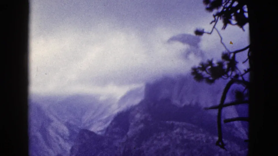 1953 California frame showing a misty granite mountain face, likely Yosemite scenery, with pine branches silhouetted along the side.