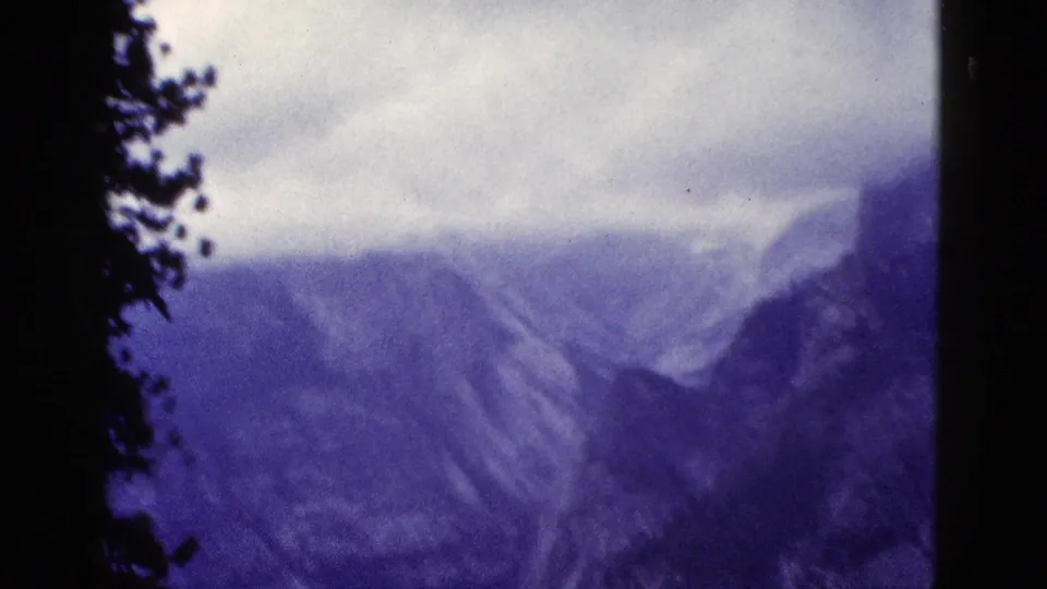 1953 California 8mm frame showing a soft, clouded mountain vista with pine silhouettes along the left side.
