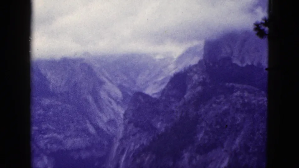 1953 California 8mm frame of clouded mountain ridges with a dark foreground trunk and heavy color aging.