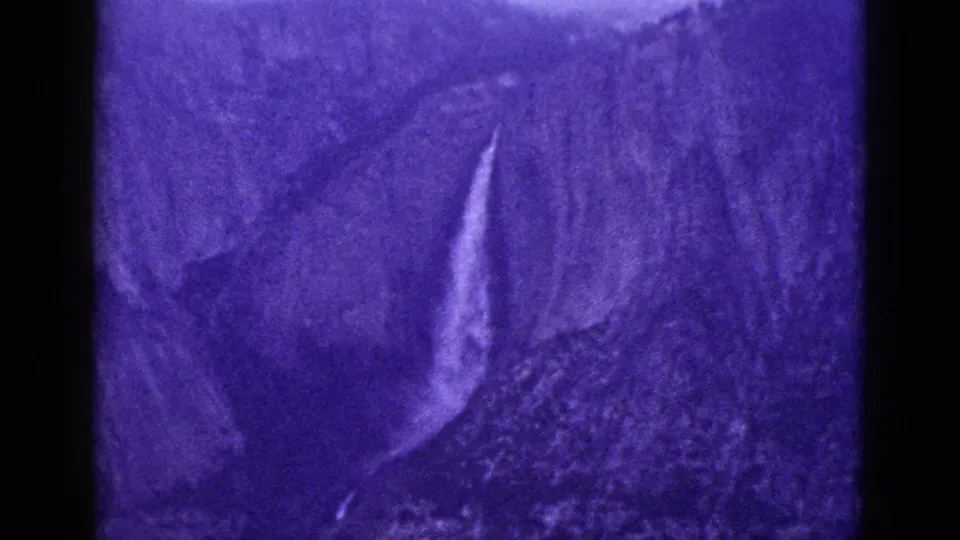 1953 California 8mm frame with a bright waterfall cutting through a dark, rugged mountainside under heavy purple color shift.