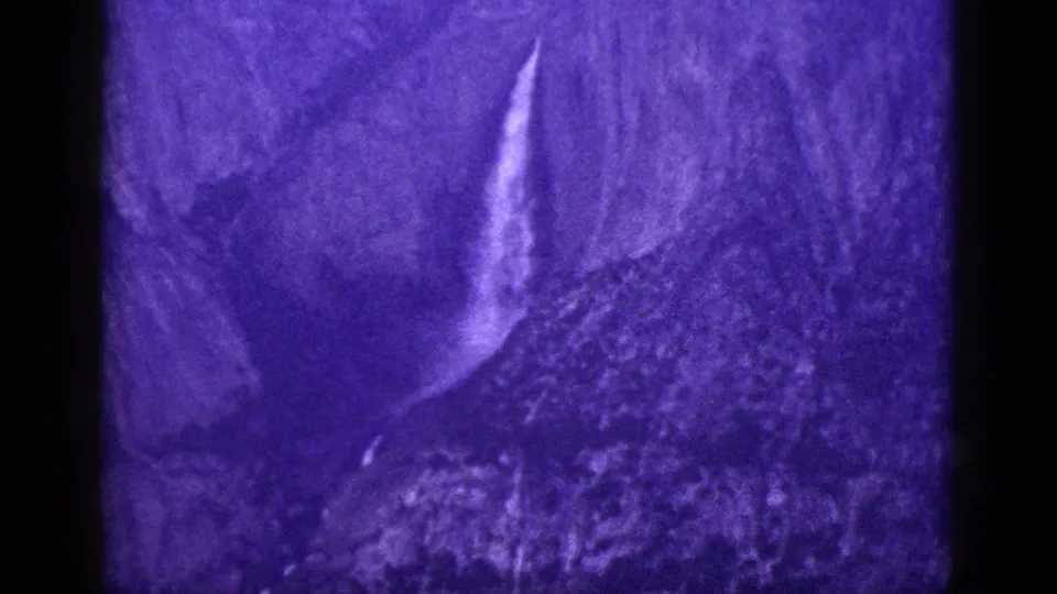 Purple-tinted 1953 California home-movie frame showing the waterfall lower on the steep rock face with visible grain and soft focus.