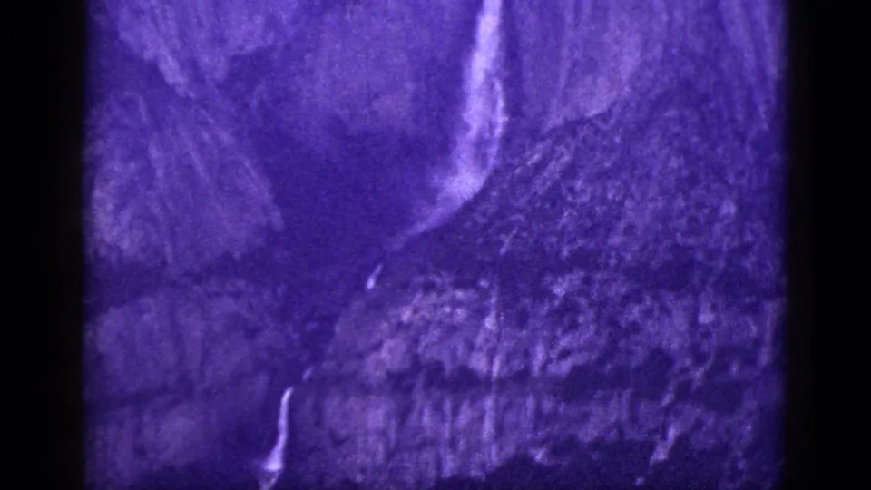 1953 California archival frame showing a pale waterfall on a shadowed mountainside, with rounded 8mm edges and strong purple tint.