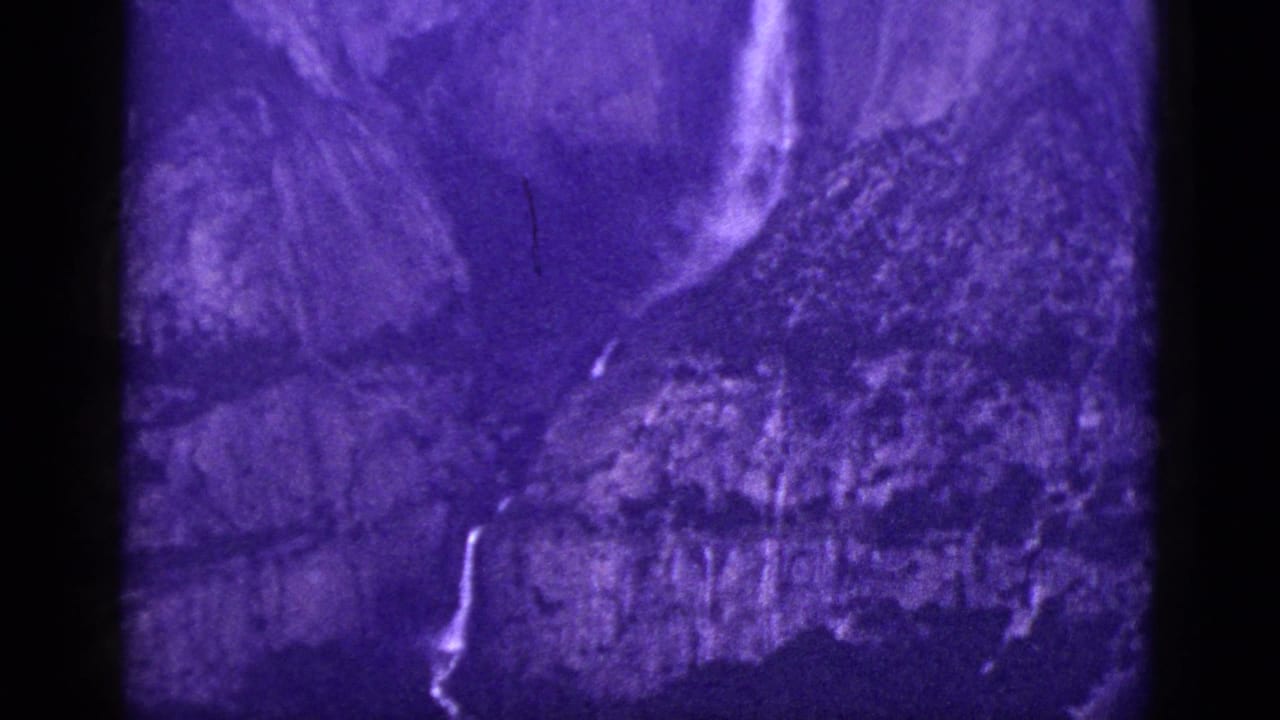 Purple-tinted waterfall running down a rugged rock face.