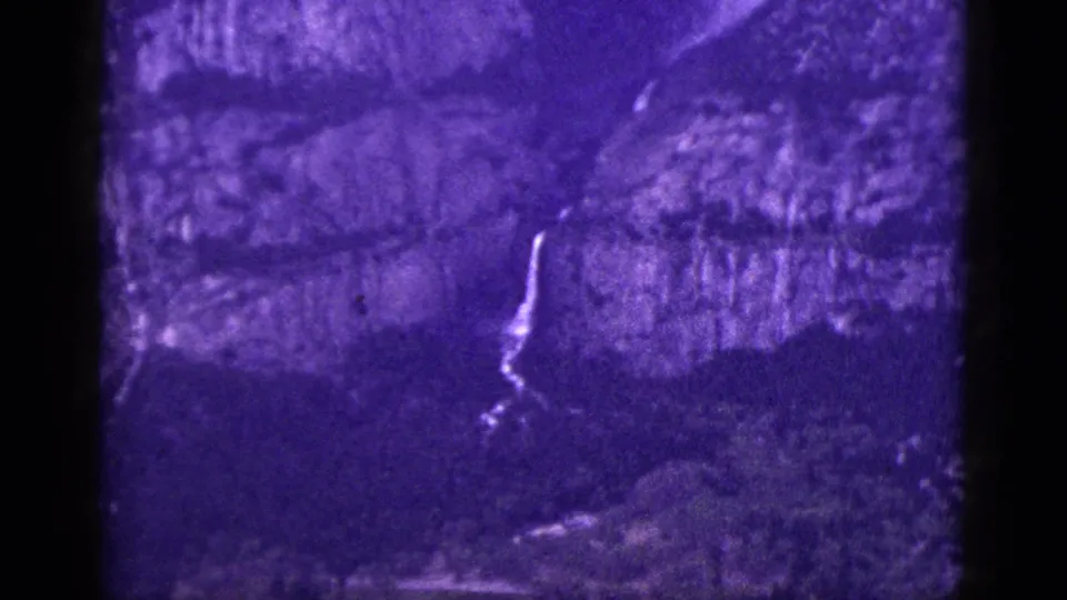 Vintage 8mm view of a waterfall crossing a shadowed California mountain face, with visible grain and dark frame borders.