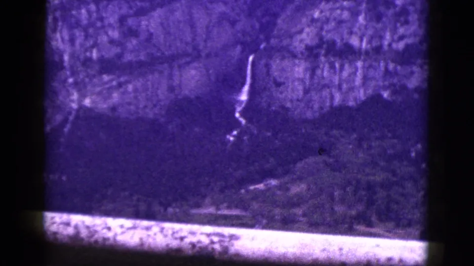 1953 California home-movie frame showing the lower cliffside waterfall area, tinted purple and bordered by the film frame.