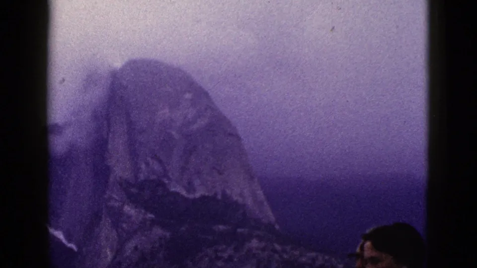 1953 8mm California footage shows a hazy mountain peak, with part of an adult face entering at the right edge.