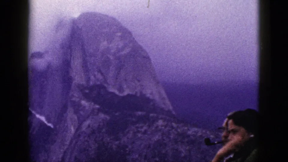 1953 8mm California footage shows a man in the lower right foreground holding a pipe as a misty mountain peak rises behind him.