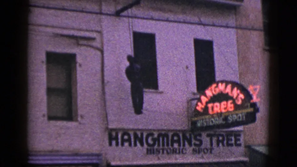 1953 California 8mm frame showing the Hangman's Tree Historic Spot sign on a building facade, with a dark hanging figure shape near a window.