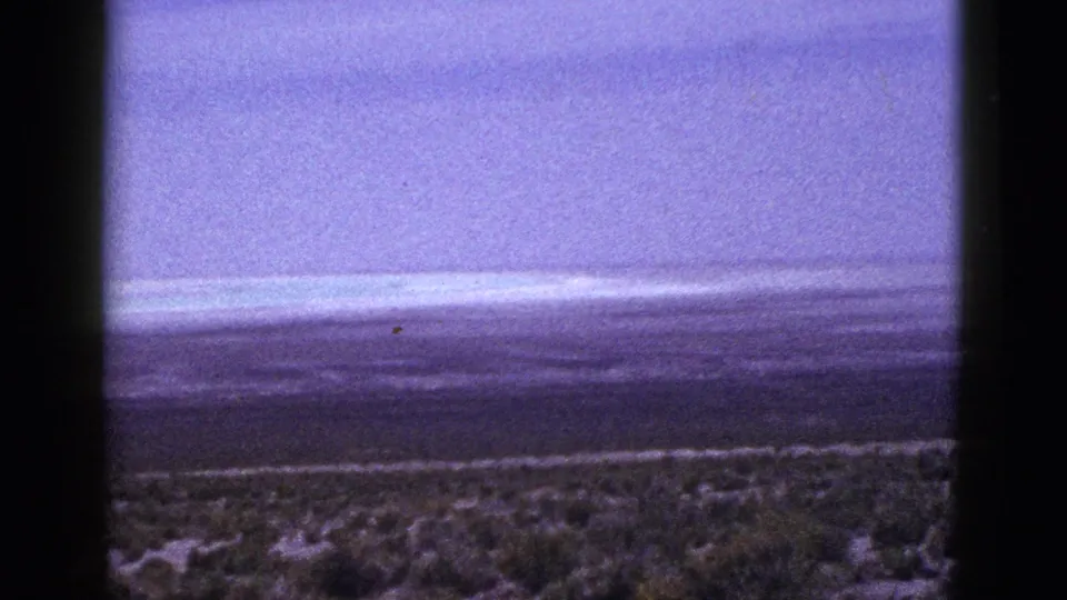 Wide 1953 California home-movie view across open shrubland toward a hazy horizon under a purple-shifted sky.