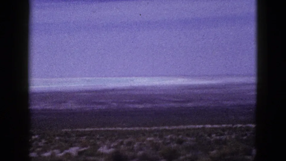 1953 California 8mm landscape frame with low shrubs in the foreground, distant horizon, and visible film-gate edges.
