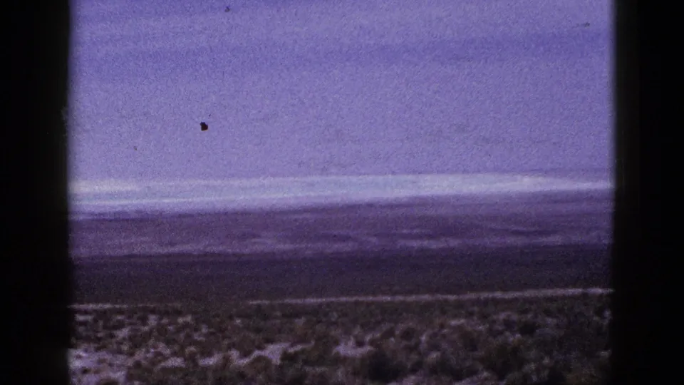 Final 1953 California 8mm frame of open shrubland and hazy sky, with visible grain, color shift, and a small film speck.