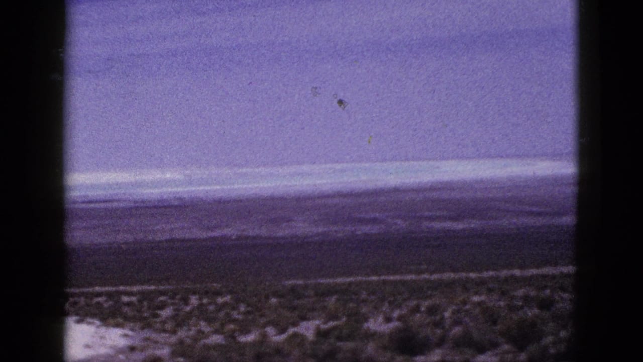 1953 California 8mm frame showing sparse desert vegetation, a low horizon, distant hills, and an overcast sky with dark scan borders.