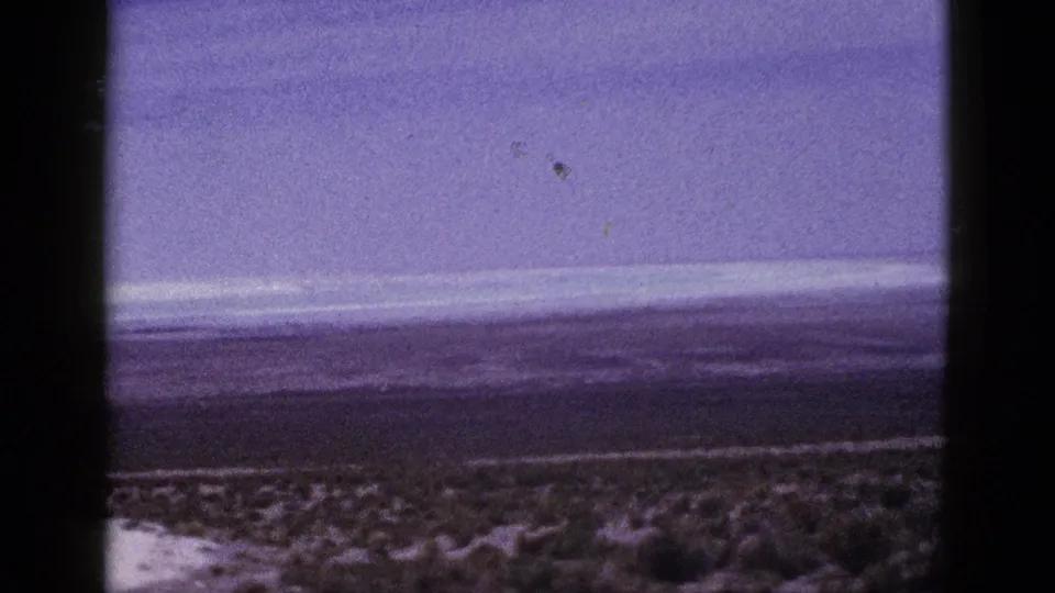 1953 California 8mm frame showing sparse desert vegetation, a low horizon, distant hills, and an overcast sky with dark scan borders.