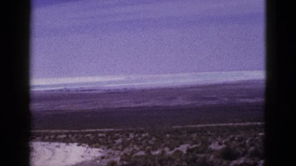 1953 California desert view with a broad sky, distant ridges, low scrub, and the vertical edge of the scanned 8mm frame.