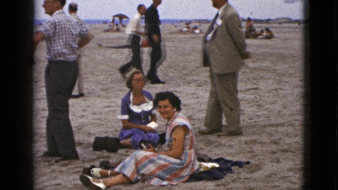 Two seated women face the camera as several men stand and walk in the background.