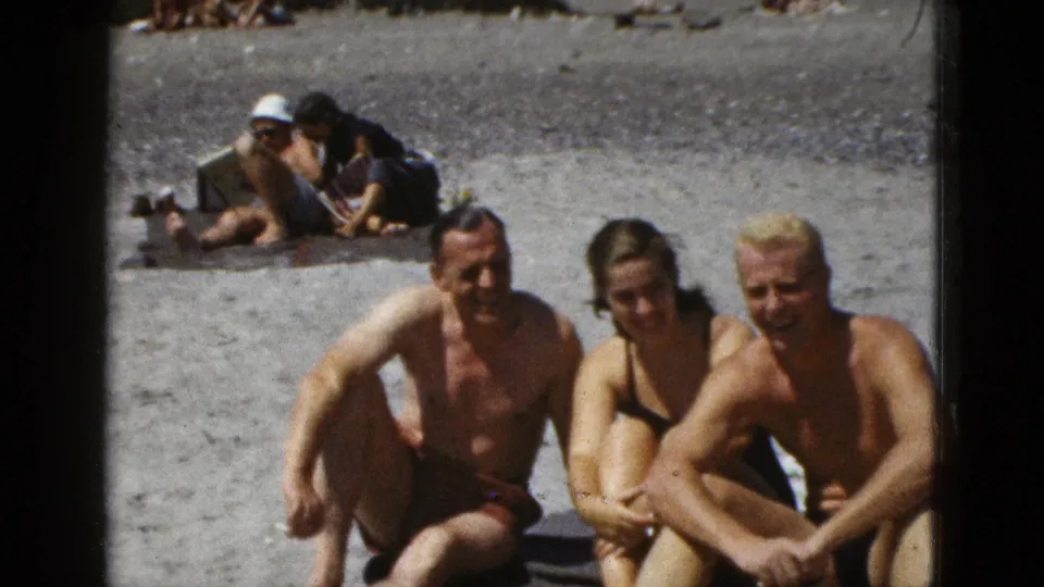 Closer 1953 California home-movie view of a man, woman, and older man seated together on a sandy beach.