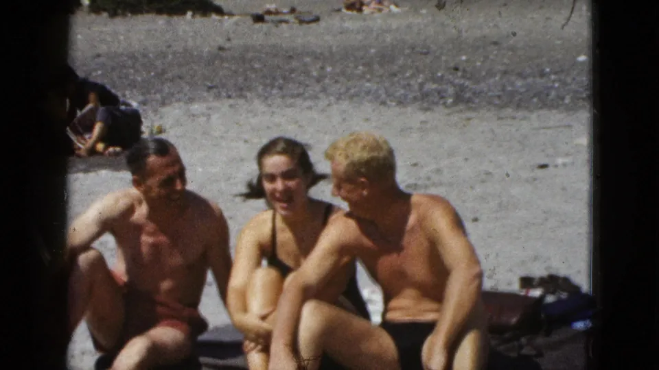 1953 California beach frame showing three adults in conversation or posing, seated close together on a towel.