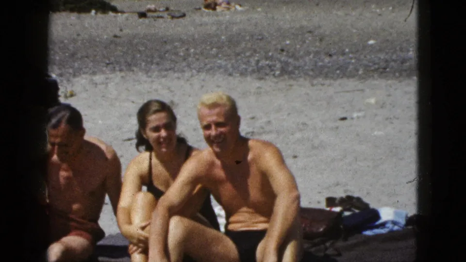 Three adults relax on a California beach in 1953, seated close together on sand in swimsuits with home-movie framing.