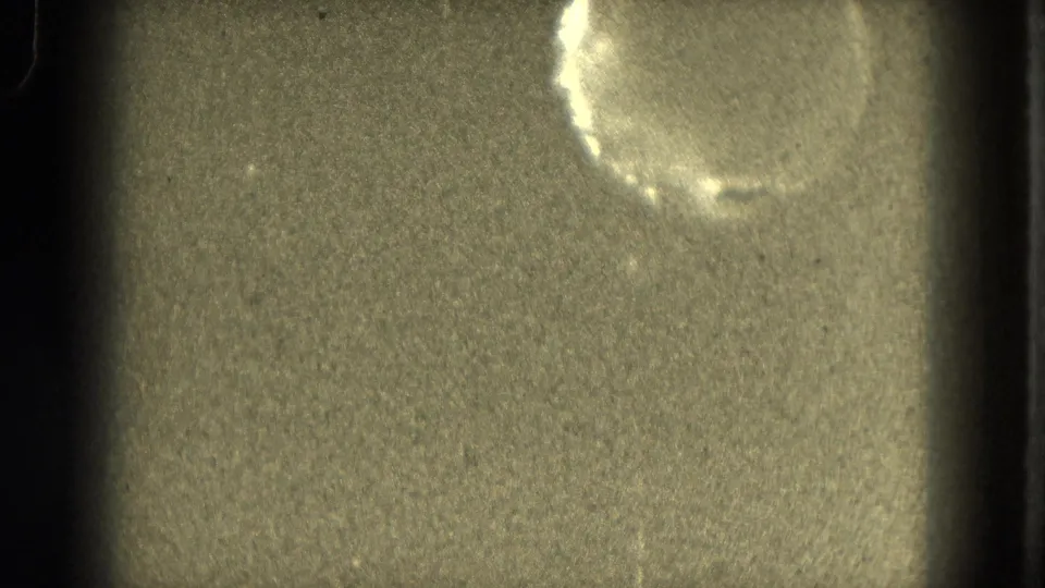 1953 8mm frame with a pale moon-like circle near the upper right, heavy grain, and dark vertical film-edge bands.