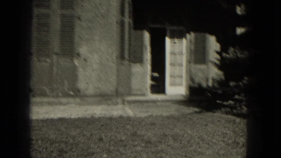 Brief exterior cutaway shows a Milwaukee house facade with louvered shutters, a doorway, lawn, and shrubs in 1953 home-movie footage.