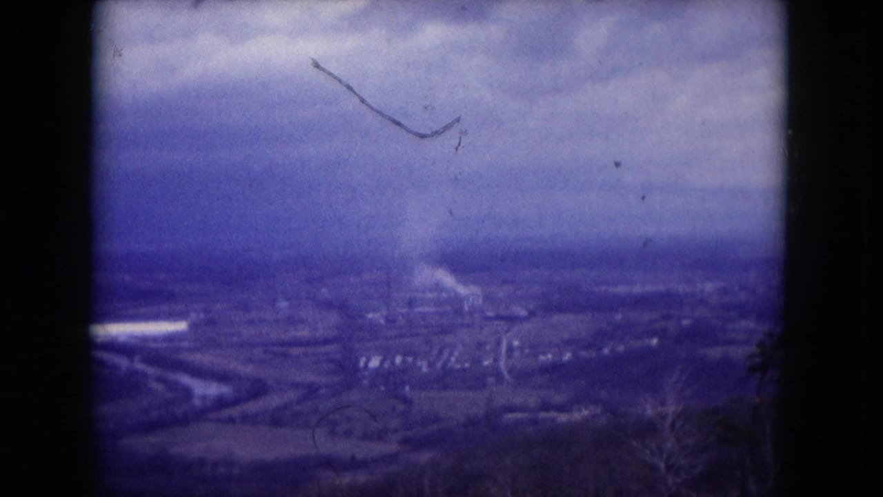 1953 Milwaukee-area 8mm frame showing a soft elevated view over a town or valley landscape with industrial smoke under gray clouds.