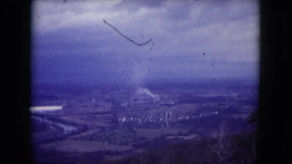 1953 Milwaukee-area 8mm frame showing a soft elevated view over a town or valley landscape with industrial smoke under gray clouds.