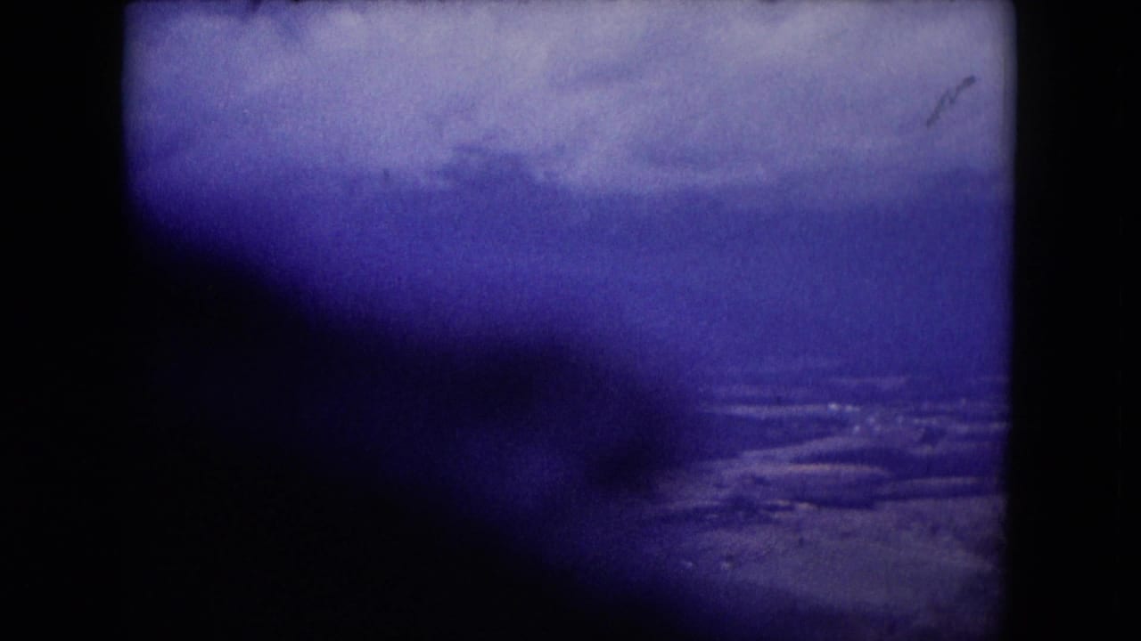1953 Wisconsin home-movie frame showing a soft blue-purple horizon over water, with dark shadowing across the lower left and rounded film edges.