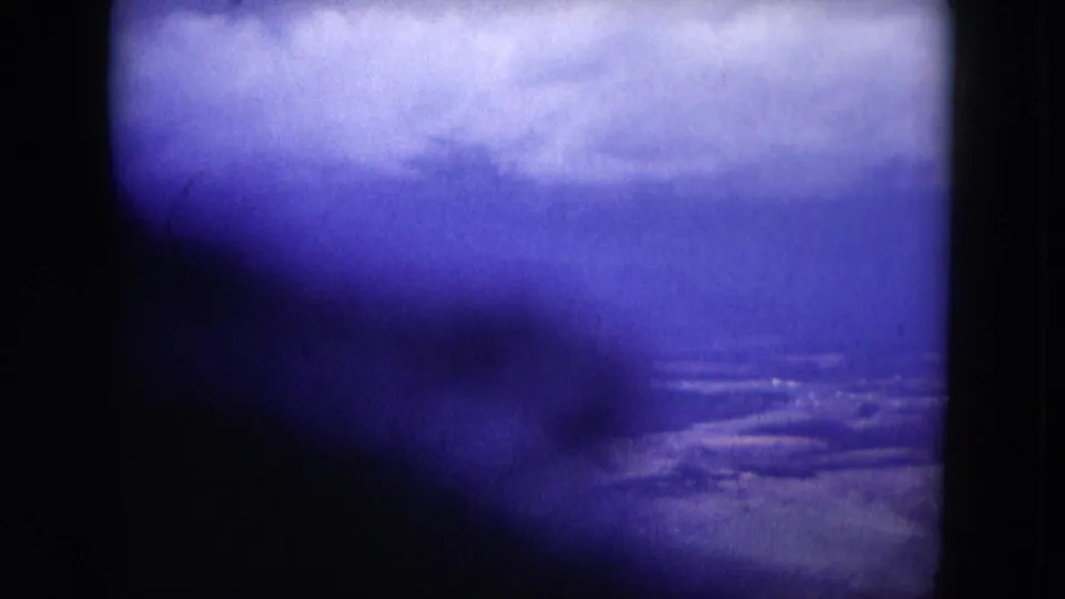 1953 Milwaukee-area home-movie frame with cloudy sky, distant water or shoreline, and a large dark shadow passing across the lower portion.