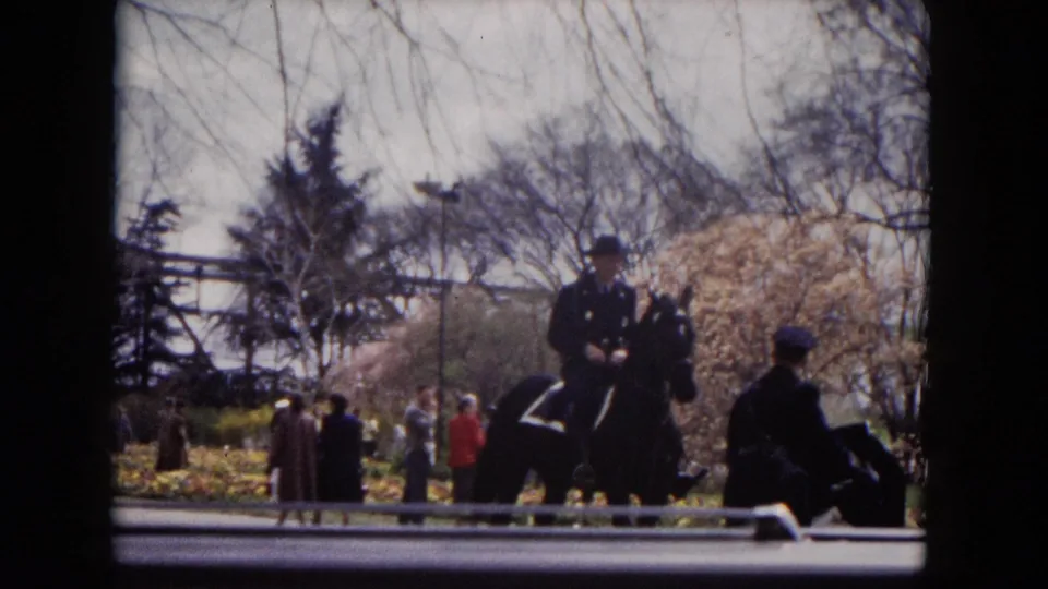A mounted police officer rides through a Milwaukee park while pedestrians stand nearby under spring trees.