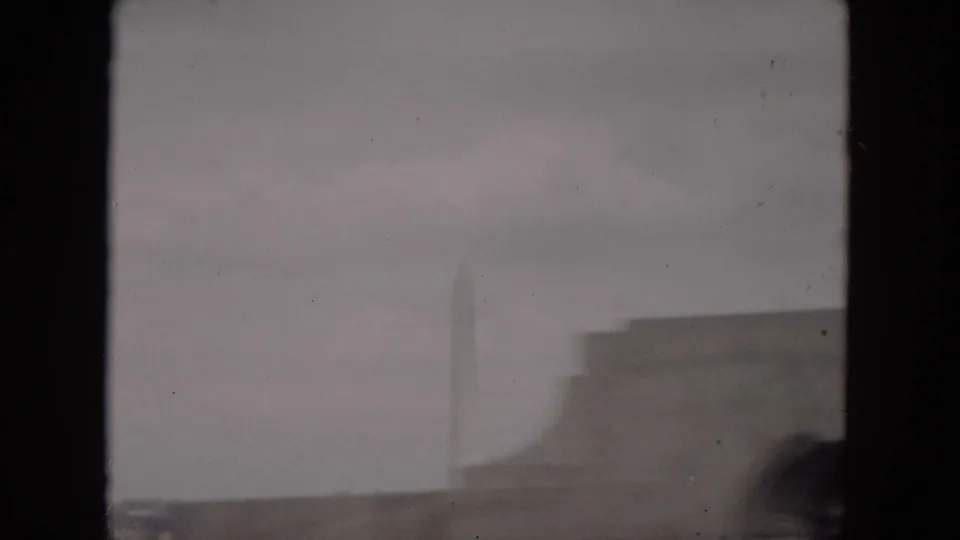 1953 Milwaukee home-movie view of a distant pale obelisk-like structure, low rooflines, and gray haze.