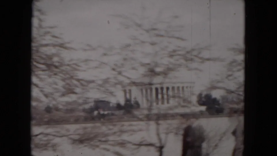 A soft 8mm view across water toward a neoclassical domed building, partly obscured by spring branches.