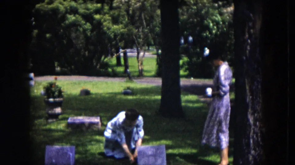 1953 Milwaukee cemetery view with one woman kneeling by a grave marker while another stands nearby holding a cup.