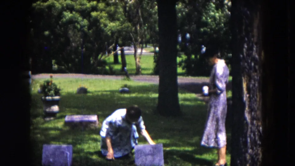 1953 Milwaukee cemetery frame showing a kneeling woman tending near a marker and a standing woman beside trees and grass.