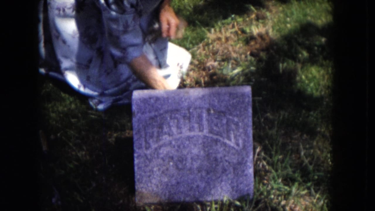 Person kneeling in grass beside a small gravestone with WILLIAM visible.