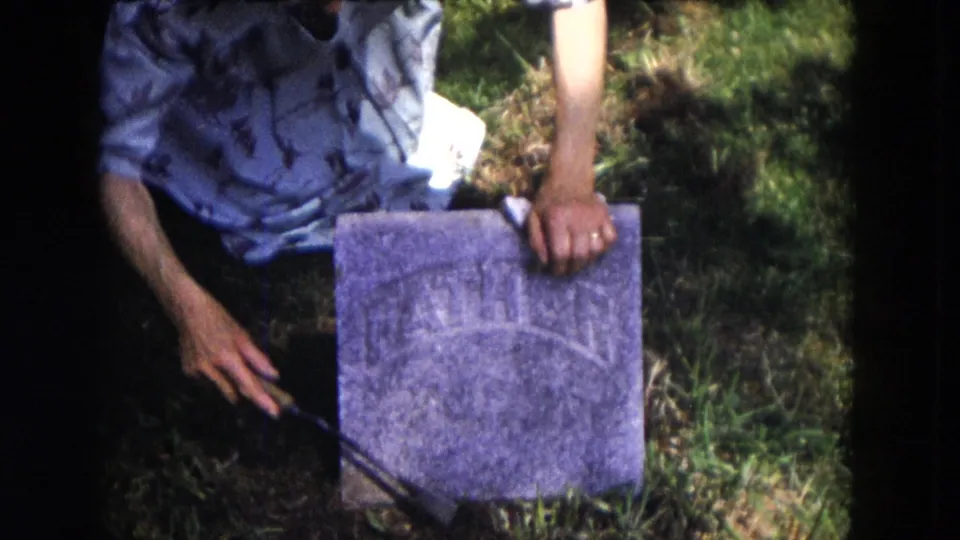1953 Milwaukee cemetery frame with a kneeling person reaching toward the ground beside a weathered WILLIAM marker.