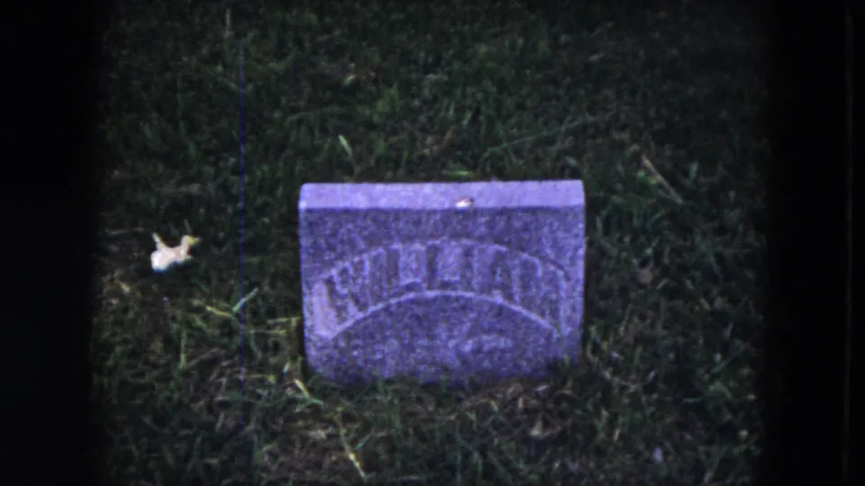 1953 Milwaukee 8mm frame of a low gravestone in grass, with partial WILLIAM engraving visible and no person in this frame.