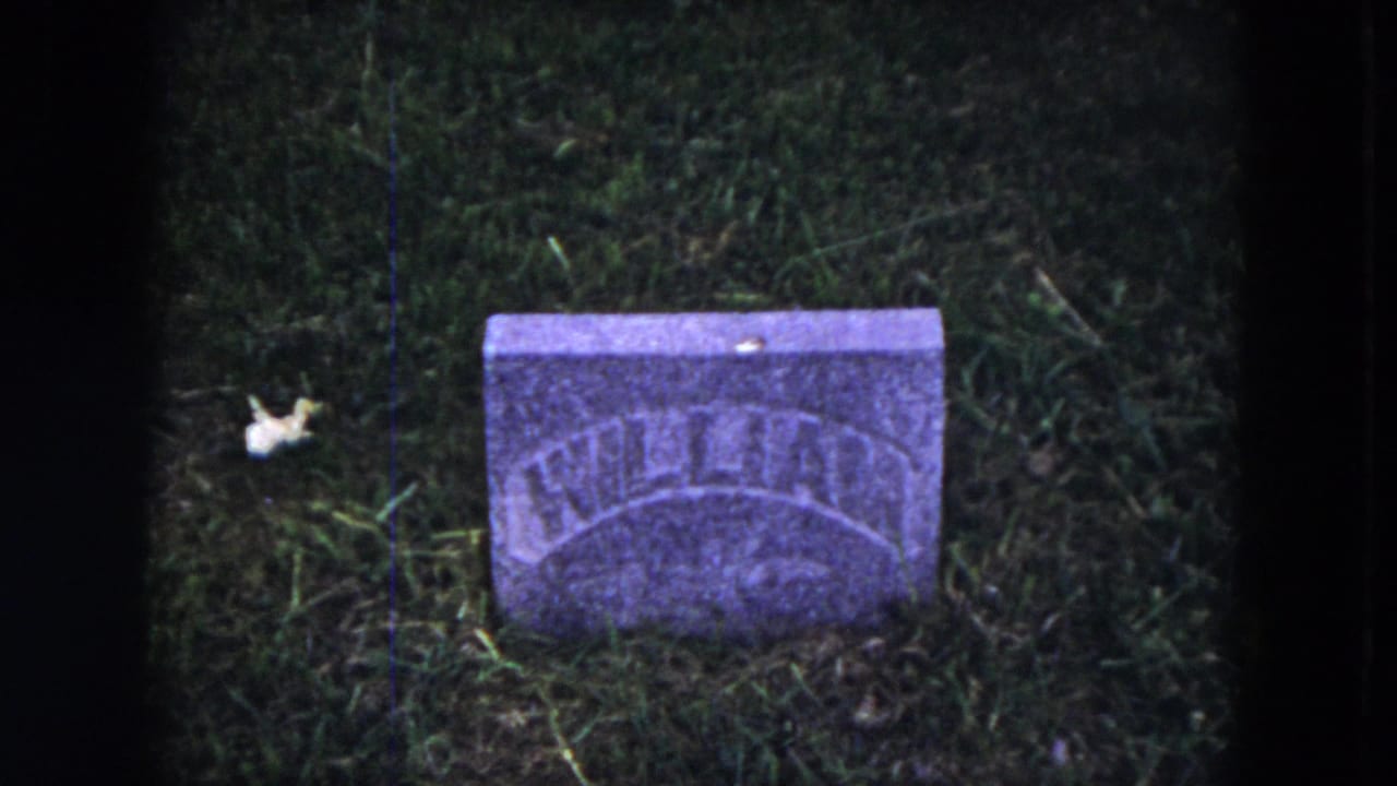 1953 8mm frame from Milwaukee metadata showing a small weathered headstone in a grassy cemetery, with arched lettering partly legible.