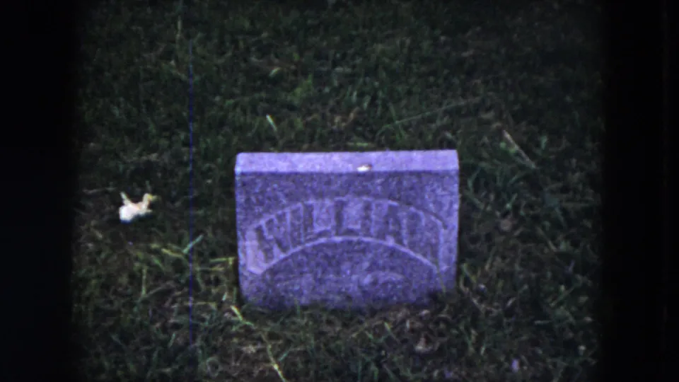 1953 8mm frame from Milwaukee metadata showing a small weathered headstone in a grassy cemetery, with arched lettering partly legible.