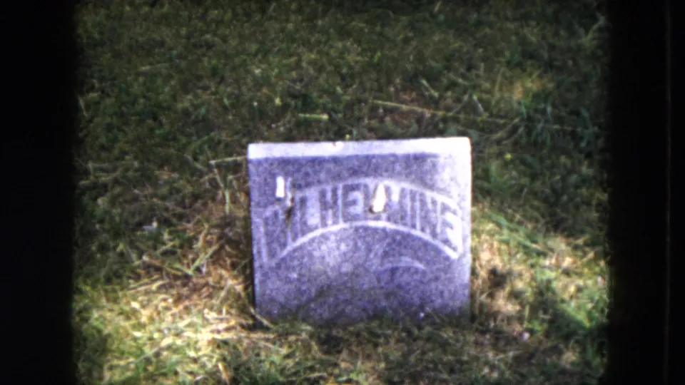 1953 Milwaukee-supported 8mm frame showing another low cemetery headstone in grass, with arched lettering and bright exposure.