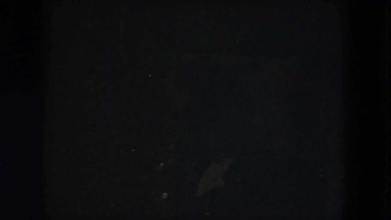 Underexposed 8mm frame from the Milwaukee home movie, showing a dark interior or window edge before the garden view becomes clear.
