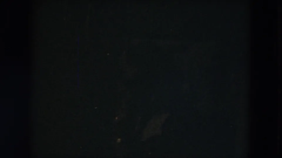 Underexposed 8mm frame from the Milwaukee home movie, showing a dark interior or window edge before the garden view becomes clear.