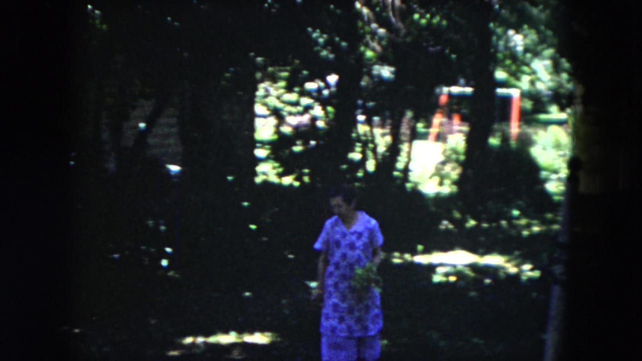 Woman in a blue flowered dress walking through a shaded garden area.