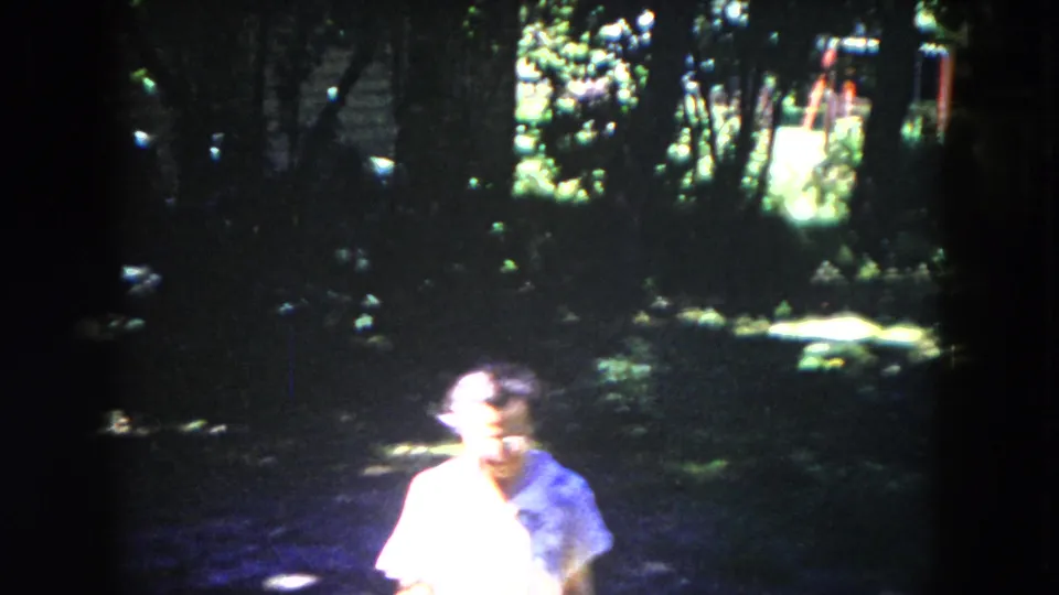 A closer 1953 home-movie frame shows the woman partly overexposed by sunlight as she passes through the garden shade.