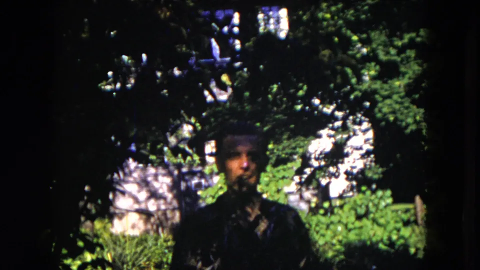 The adult man moves nearer to the camera in the 1953 Milwaukee garden scene, his face softened by shadow and 8mm focus.