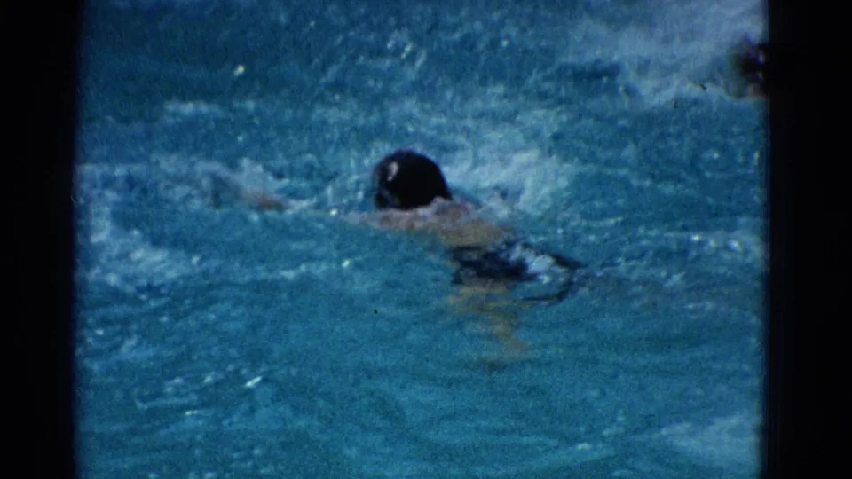 1953 Yonkers pool footage shows a swimmer moving away from camera, head low in the water amid bright splashes.