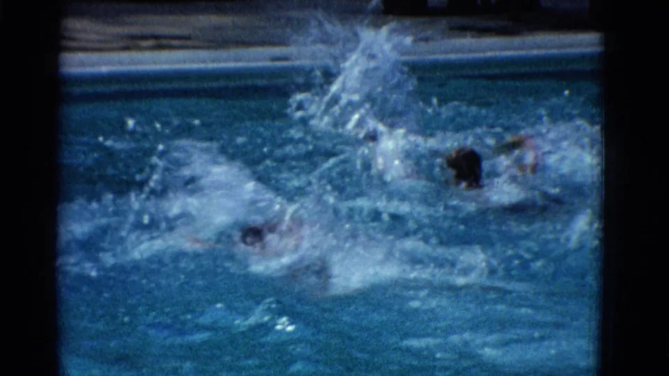 1953 Yonkers home-movie frame with swimmers partly obscured by energetic splashes in a blue swimming pool.
