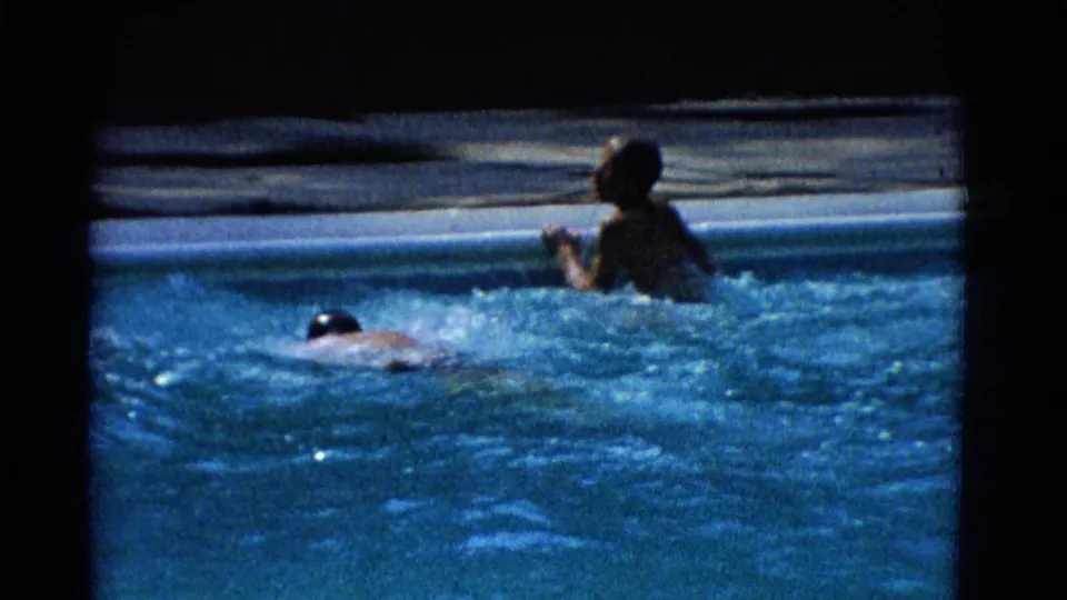 1953 Yonkers 8mm frame showing two swimmers near the edge of an outdoor pool, one upright and one moving through the water.
