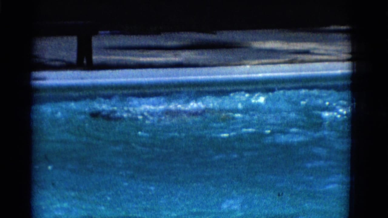 Swimmer moves through a blue pool with splashing water and dark film borders.