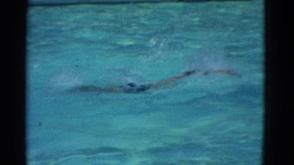 The swimmer appears elongated in the pool during a butterfly stroke in the Yonkers, New York 1953 8mm footage.