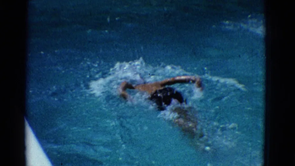 1953 Yonkers frame shows the swimmer from above in blue pool water, with a white pool edge visible at lower left.